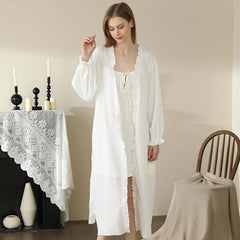 Woman wearing long white cotton lace robe, standing in a cozy room with minimal decor, perfect for home wear and loungewear.