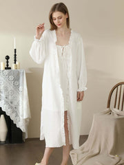 Woman wearing vintage-style white lace cotton long robe pajama set, standing in a cozy home setting